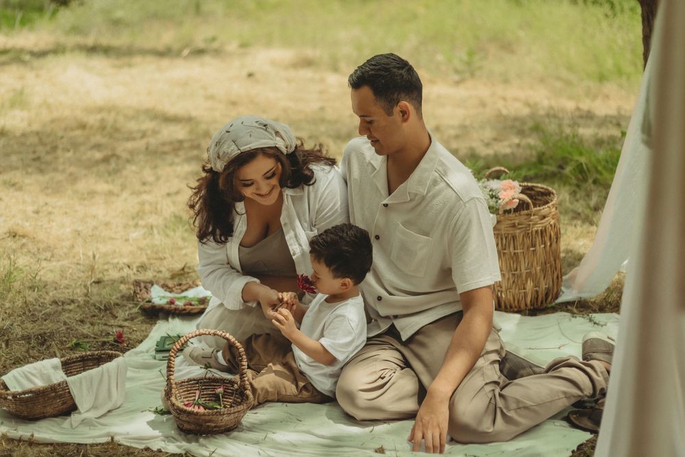 Family enjoys quality time together on a picnic blanket outdoors with woven baskets on a sunny day.