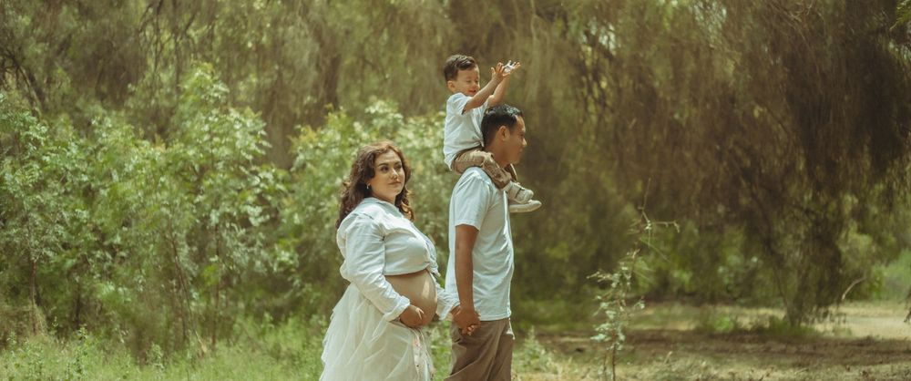 A family walks together in a sun-drenched park with lush greenery in the background during a warm afternoon in Southern California