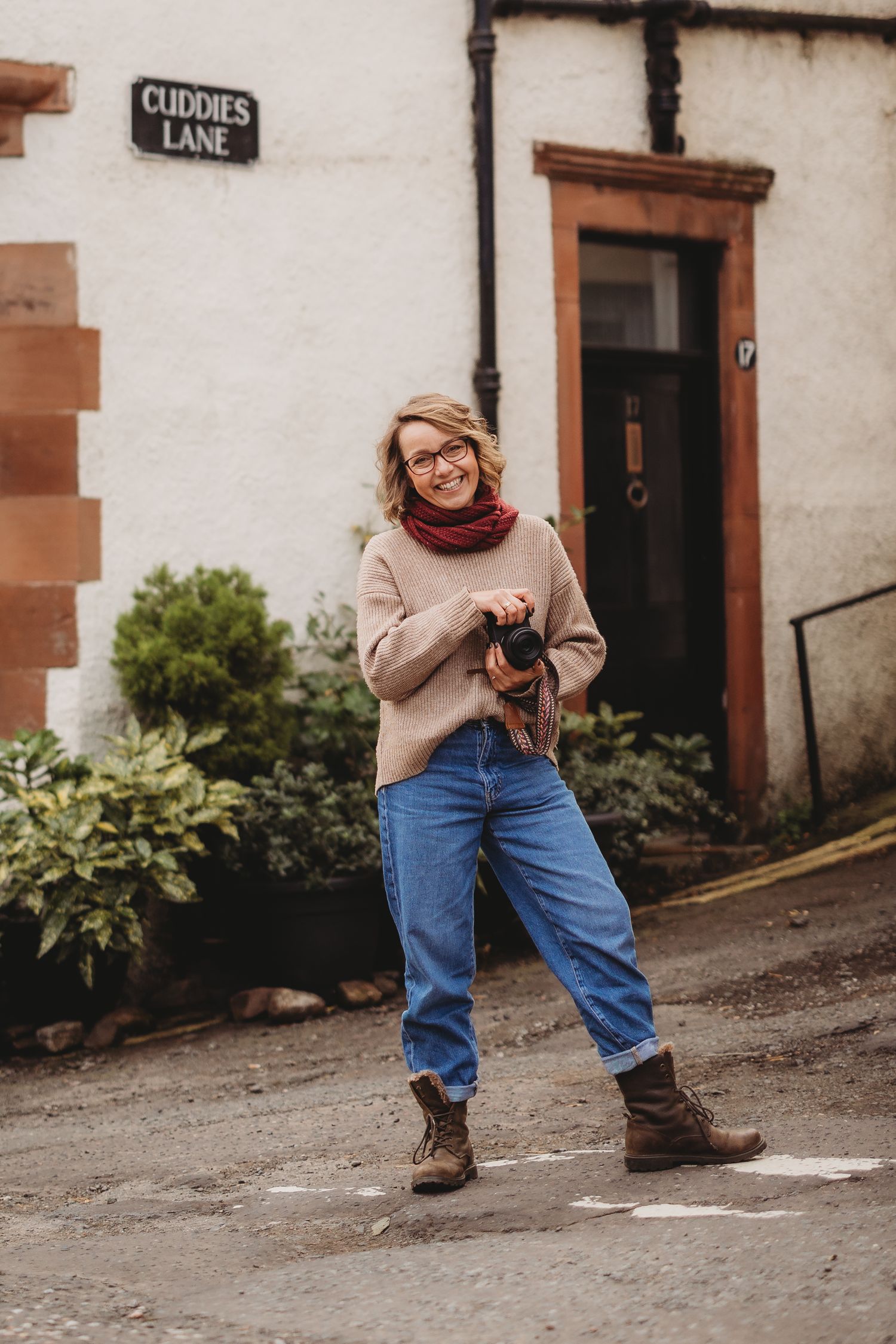 Person in a cream sweater and jeans sits casually on a wooden pier overlooking a rocky beach on an overcast day.