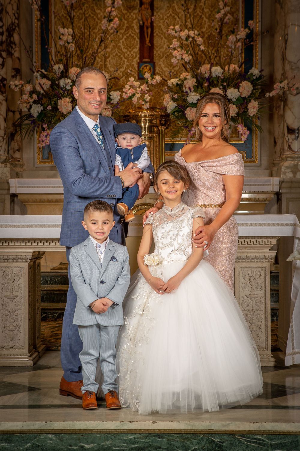 Family portrait in formal attire against ornate backdrop with floral arrangements at elegant venue.