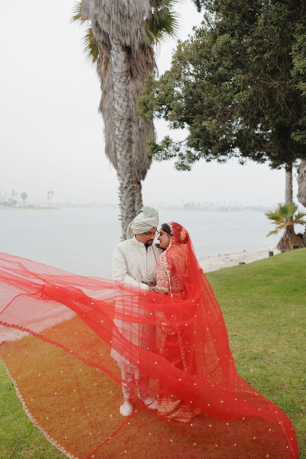 A flowing red veil billows in the wind along a palm tree-lined coastal path.