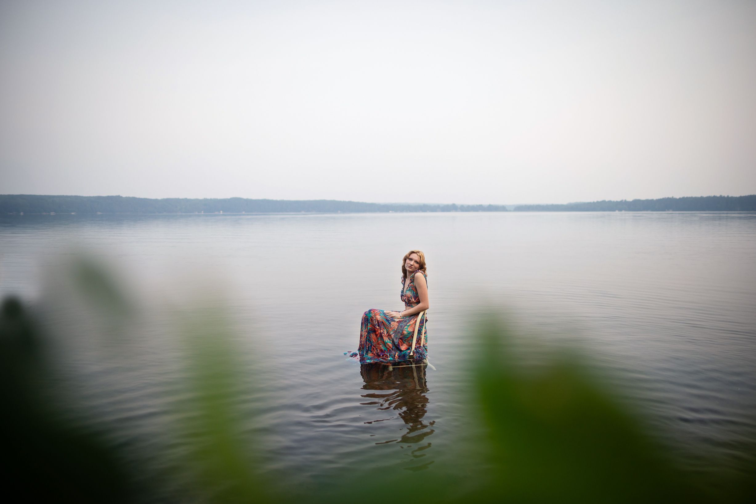 Serene misty lake landscape with a lone figure wading in calm waters at sunrise.