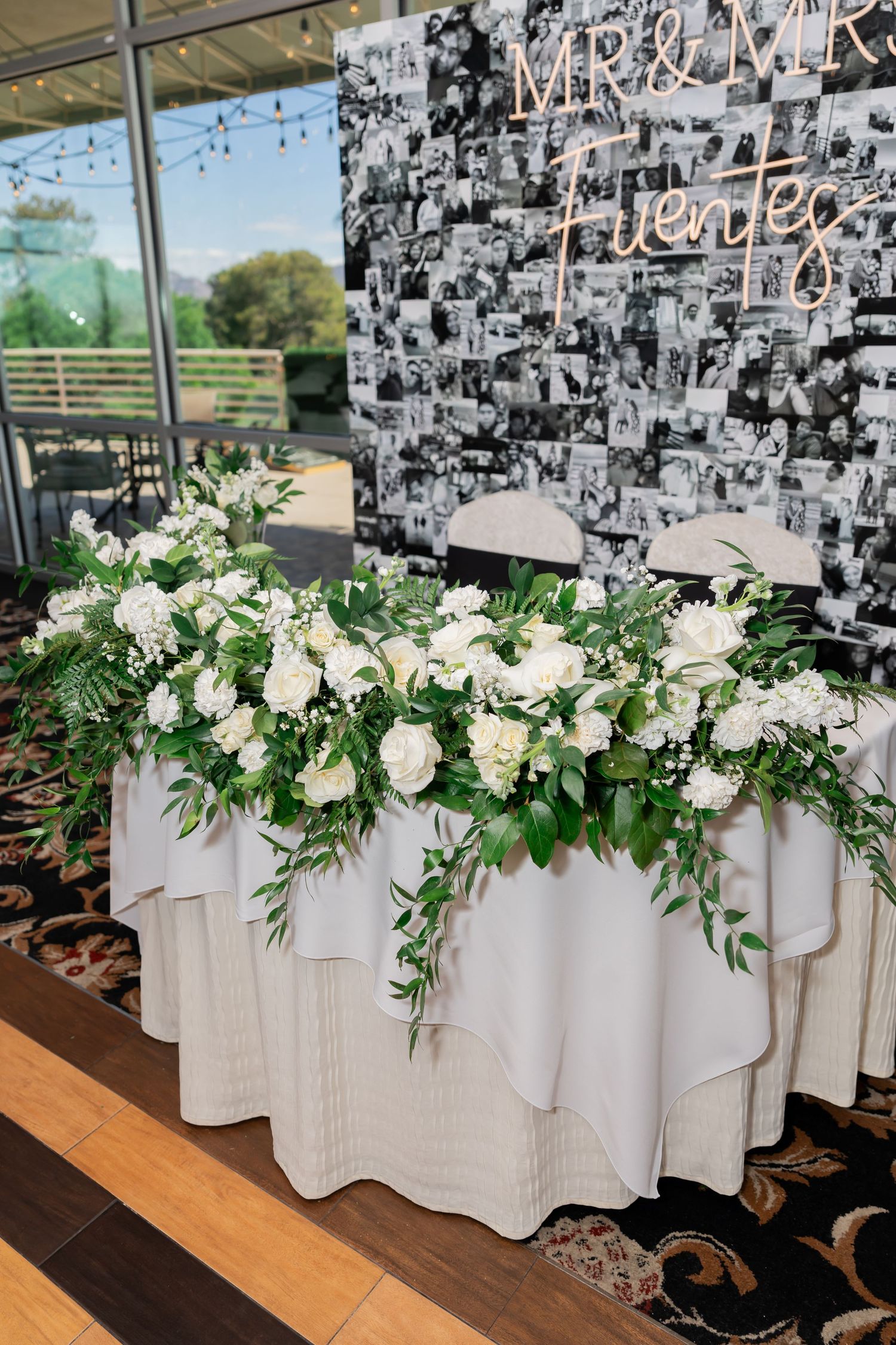 Elegant wedding sweetheart table with white roses, greenery garland, and Mr & Mrs Fuentes neon sign backdrop.