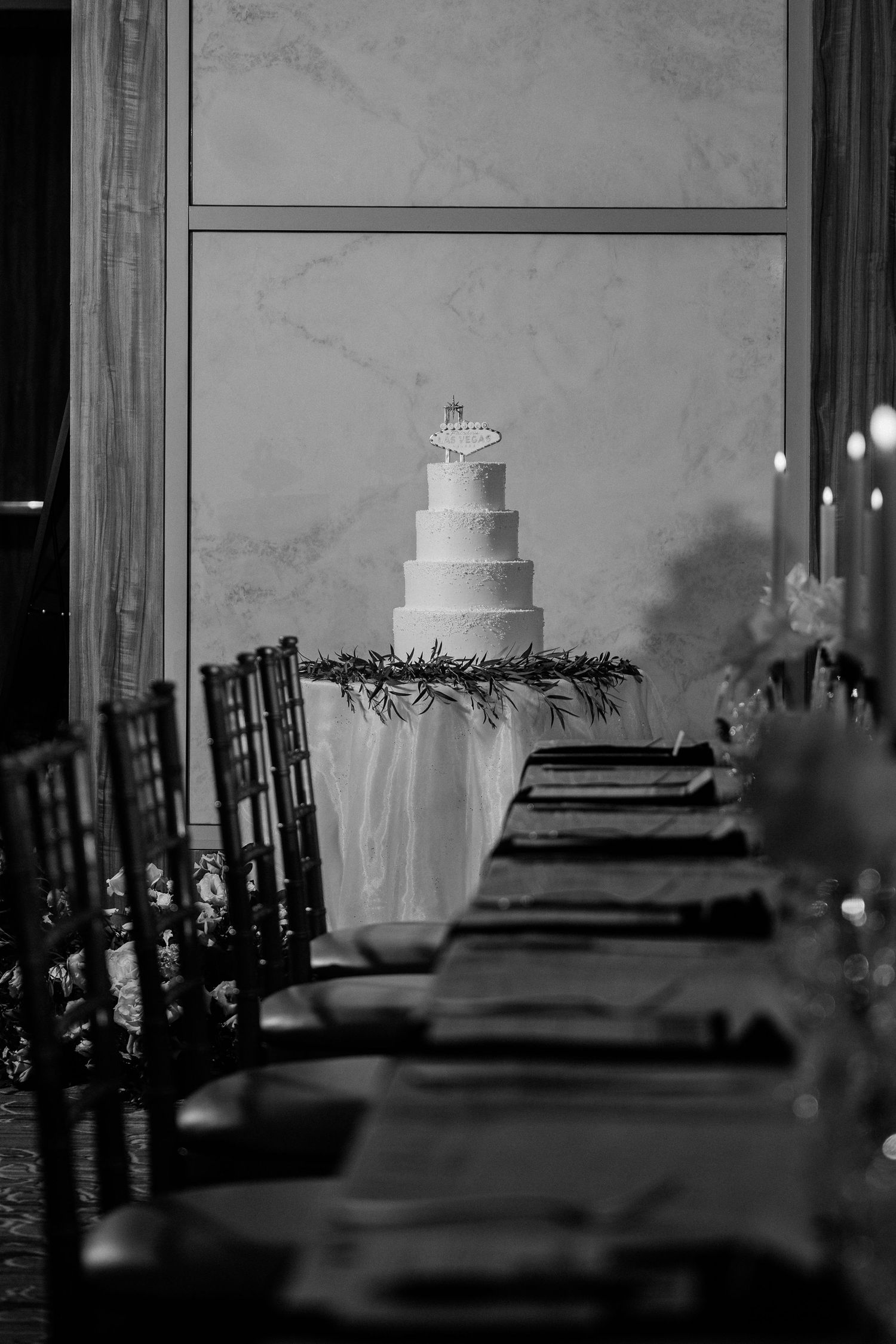 Black and white photo of an elegant wedding reception with a tiered cake centerpiece and candlelit dining table.