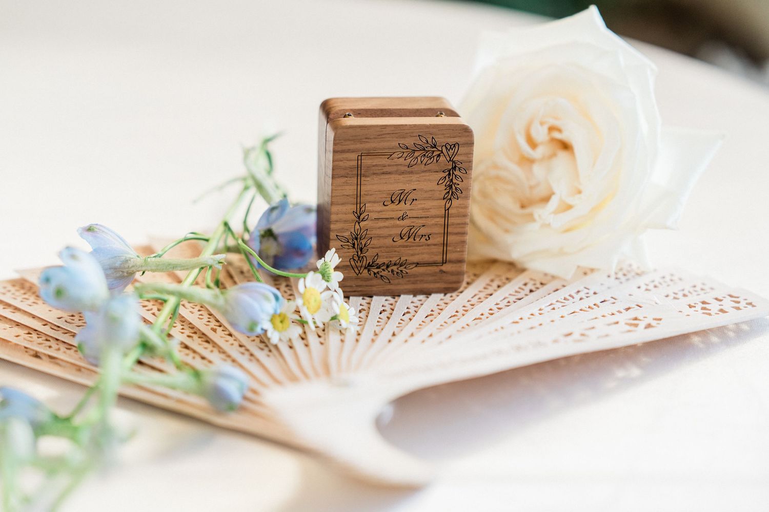 Elegant wedding ring box on a decorative fan with white rose and blue wildflowers, perfect for rustic wedding decor.