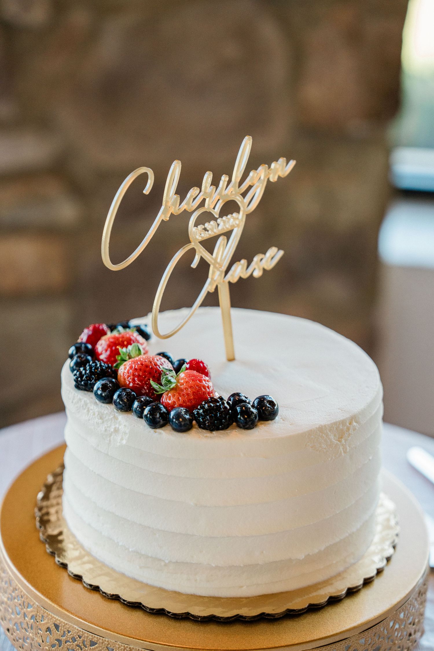 White wedding cake with fresh berries and gold laser-cut topper reading Cherilyn and Chase.