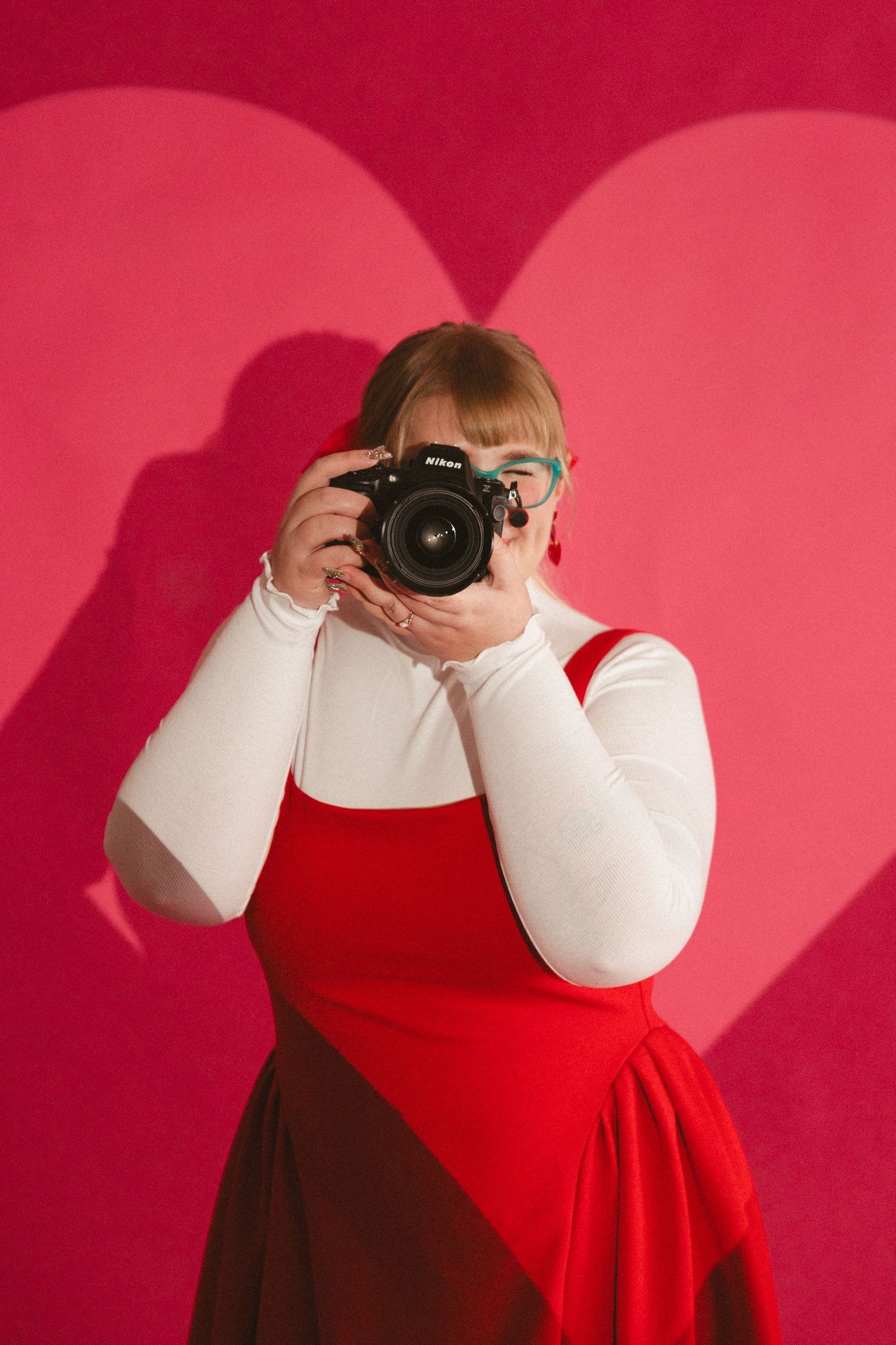 Photographer wearing colorful rainbow striped sweater and teal glasses reviews photos on digital camera.