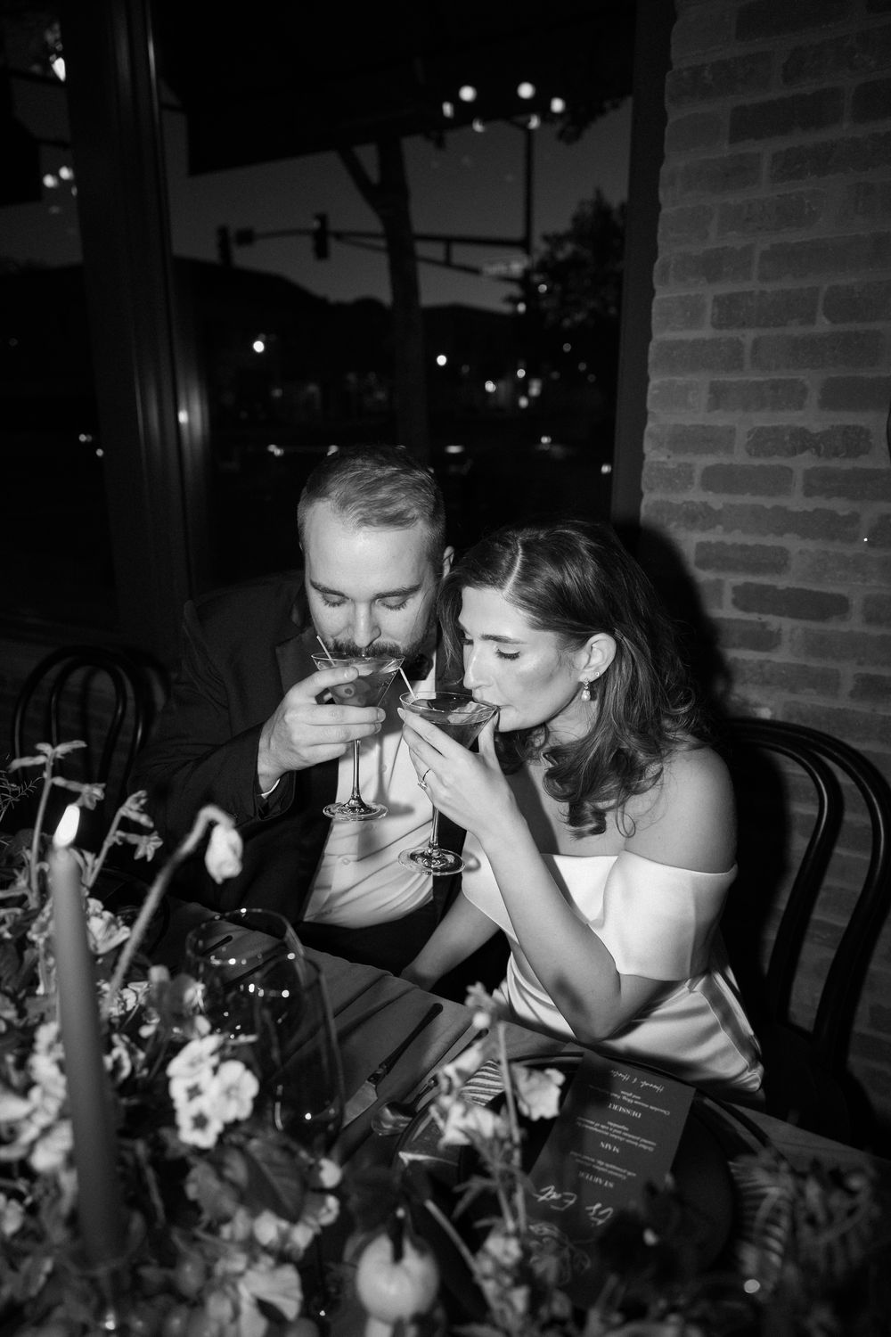 Black and white photo of bride and groom sharing cocktails at candlelit wedding reception table.