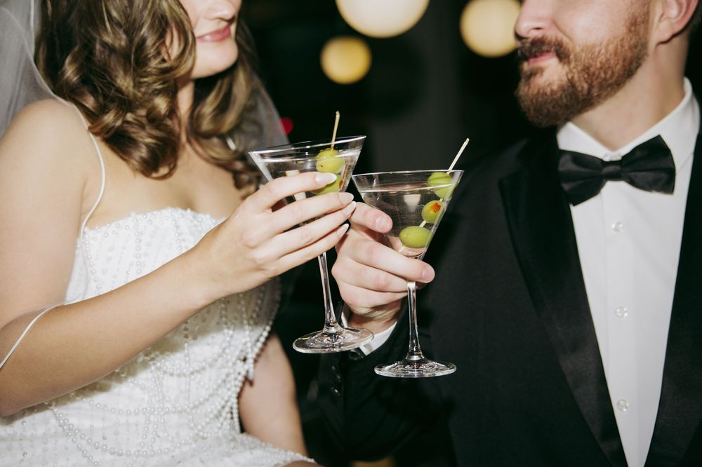 Bride and groom clinking martini glasses with olive garnishes at wedding reception.