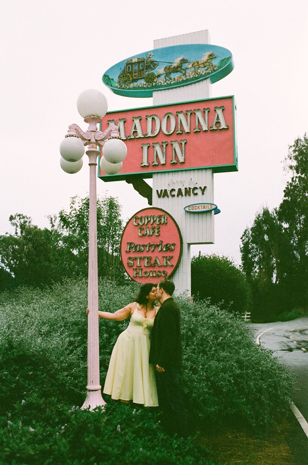 Couple kissing under the iconic Madonna Inn sign with vacancy notice in San Luis Obispo, California.
