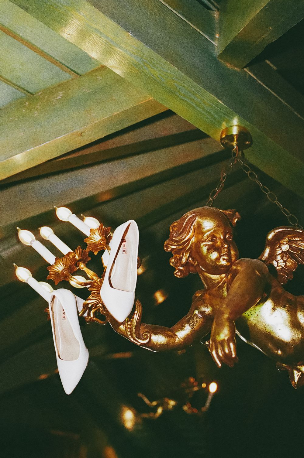 Vintage ceiling fan with cherub decorative elements and light fixtures mounted on wooden beams in warm lighting.