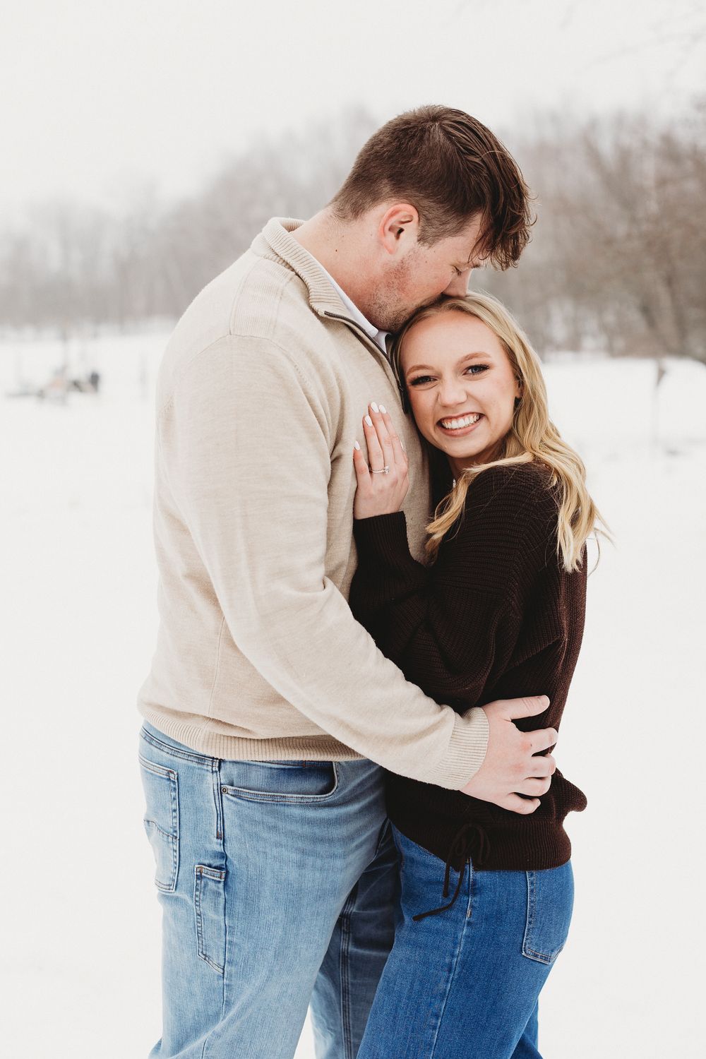 Snowy engagement photo in Maine with couple embracing in winter landscape at sunset