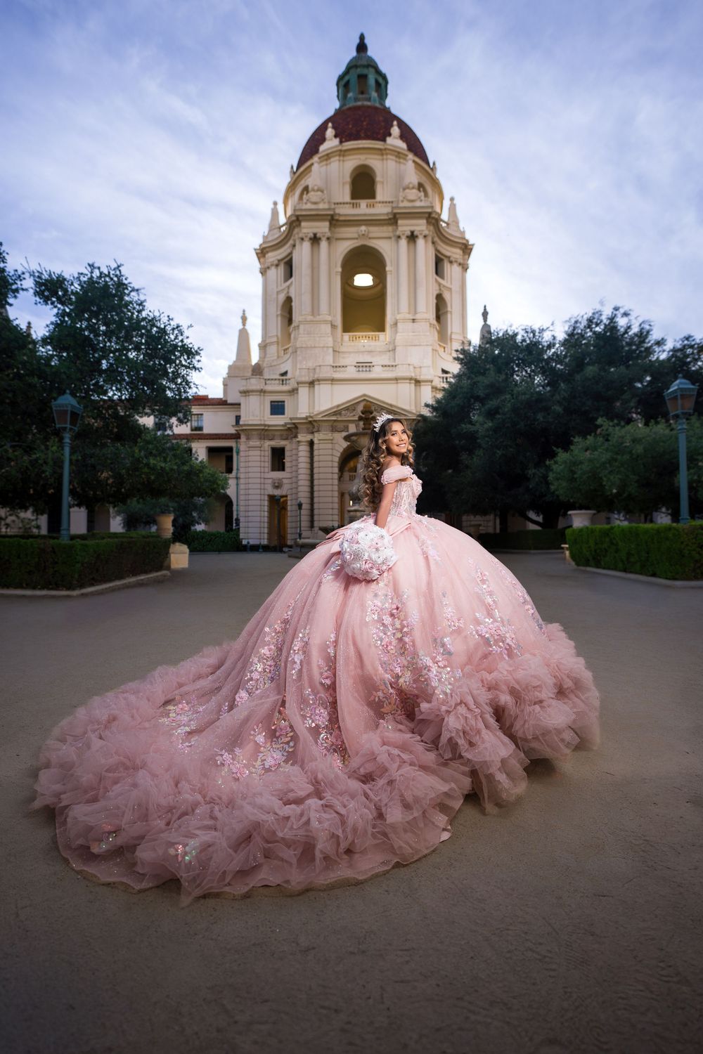 Young woman in a pink ballgown quinceañera dress poses before Pasadena City Hall at dusk.