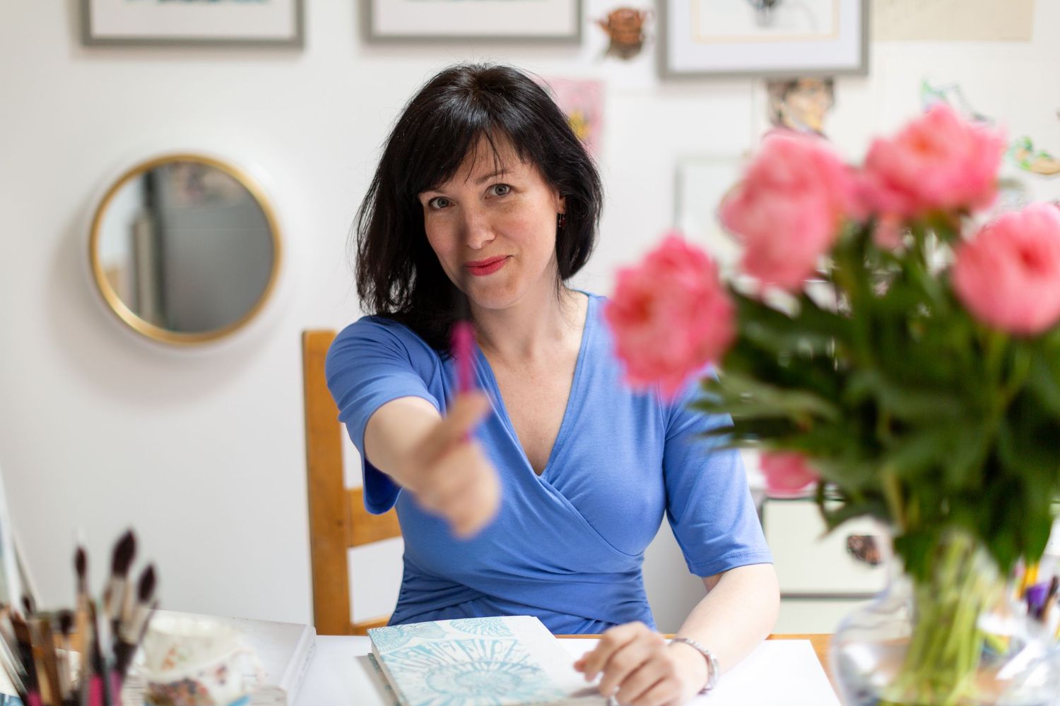 Artist sits at desk with pink flowers and art supplies.