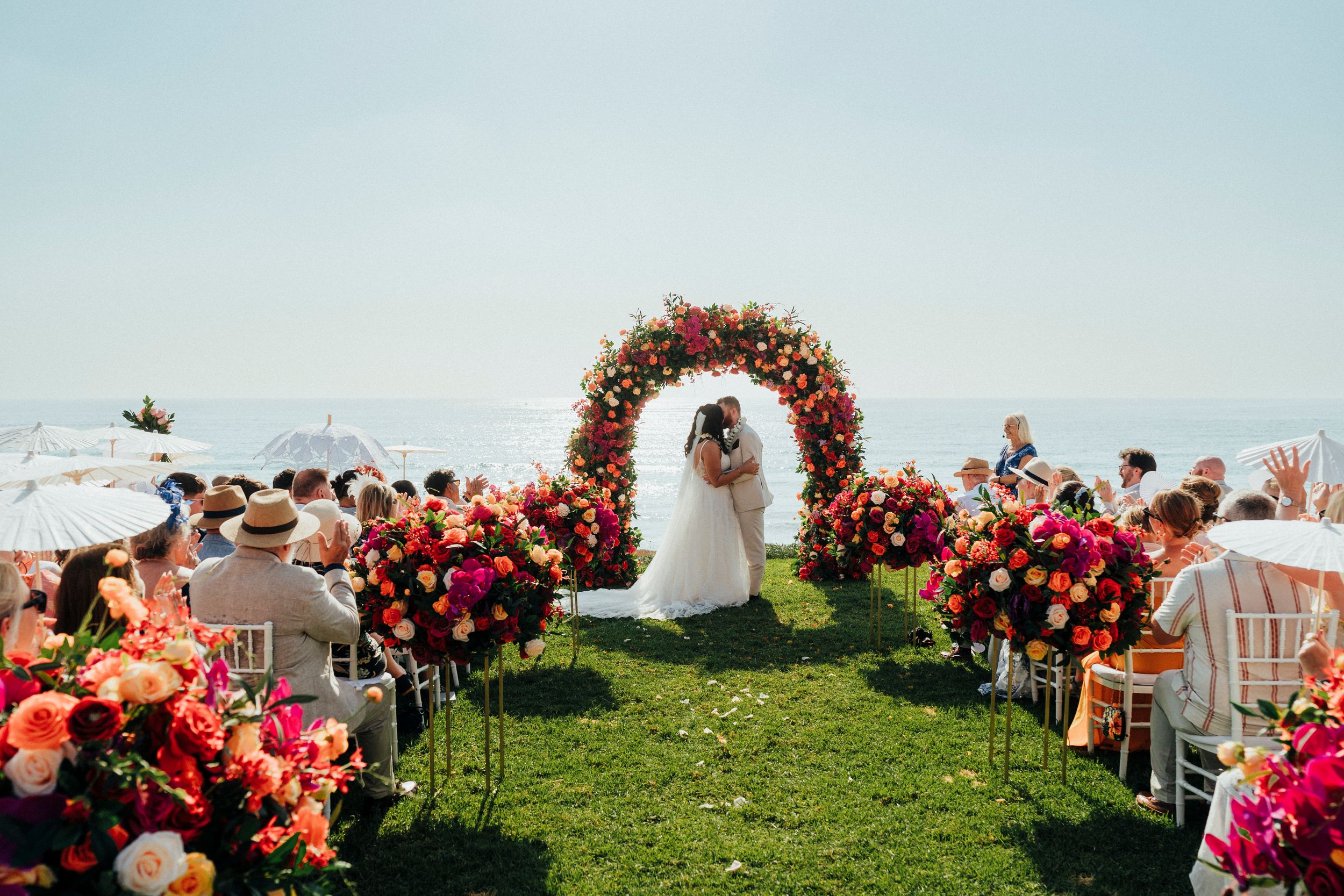 Panoramic view of an outdoor wedding ceremony setup with floral arrangements and white chairs on a grassy hilltop.