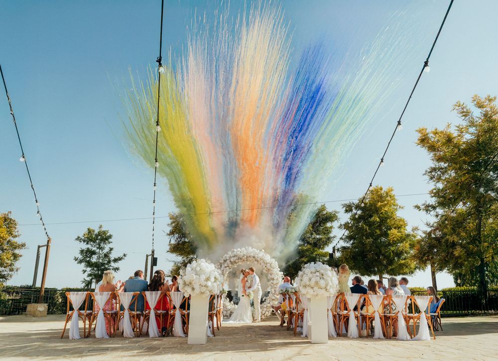 Colorful powder explosion creates a rainbow effect during a group photo shoot outdoors on a sunny day.