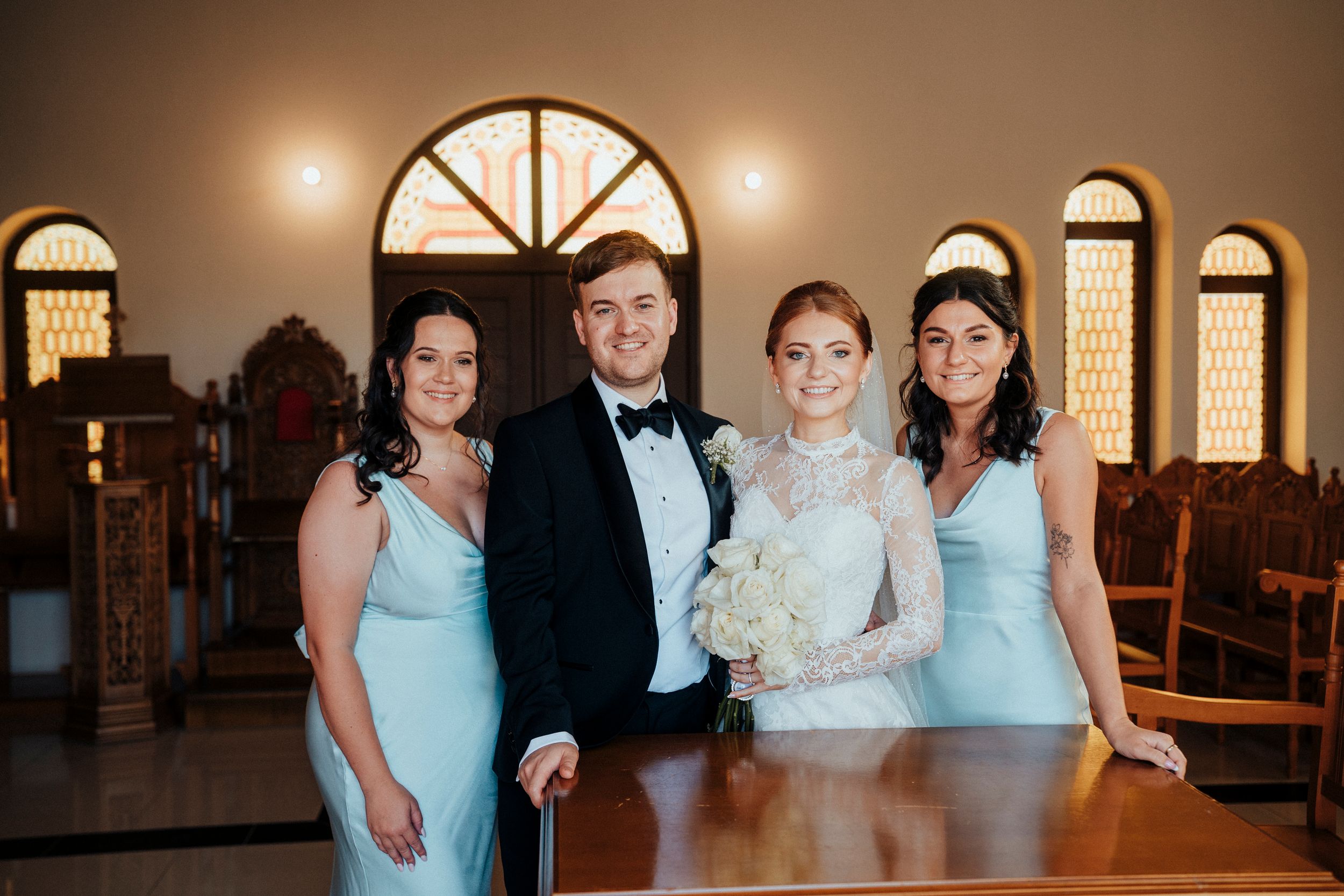 A wedding party poses in formal attire with bridesmaids wearing light blue dresses and groomsmen in black tuxedos.