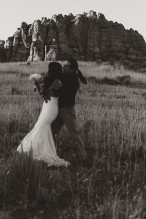 A couple dancing in a field with dramatic rock formations in the background.