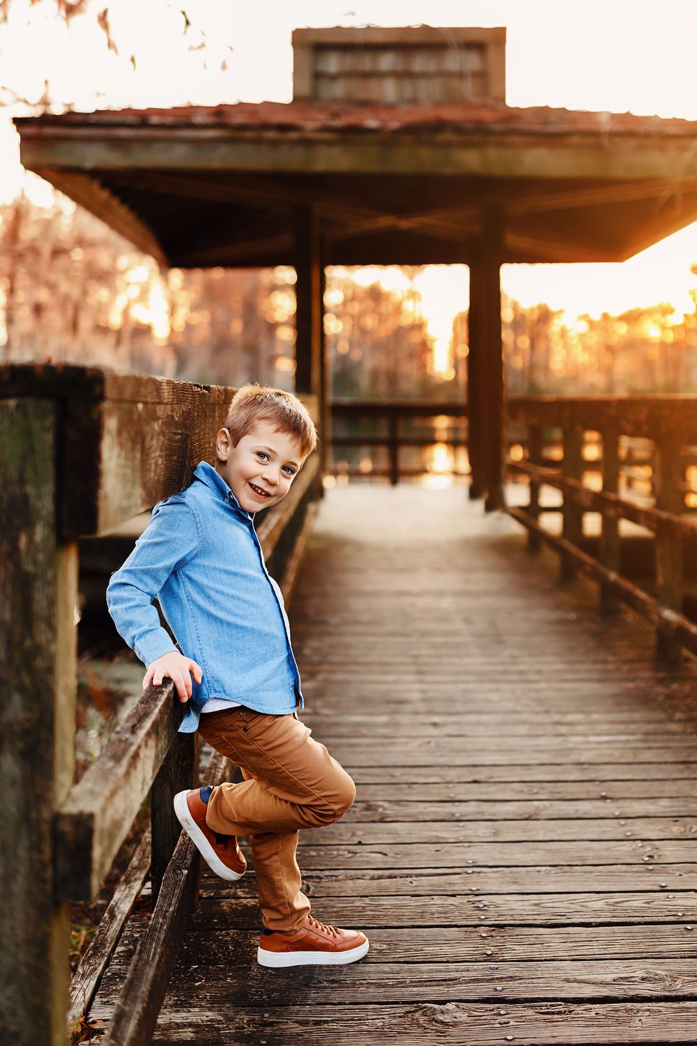 A child in a blue sweater and brown pants sits on a wooden boardwalk at sunset creating a warm golden atmosphere.