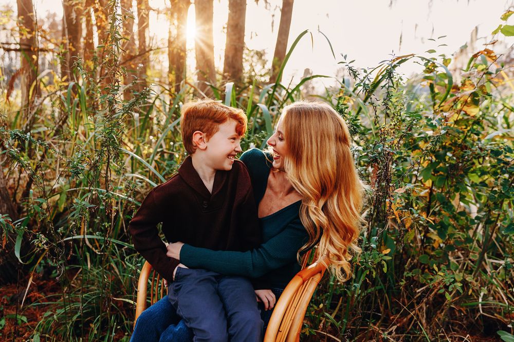 A couple shares an intimate moment in a sunlit forest setting with golden light filtering through the trees.