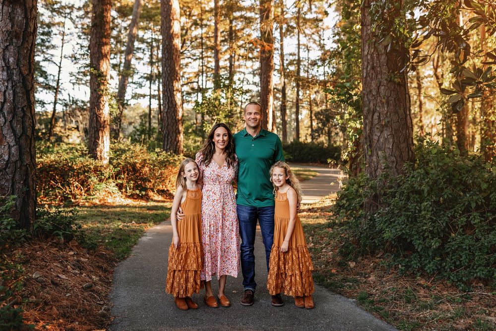 Three friends in coordinating autumn-colored dresses pose together in a sunlit forest setting.
