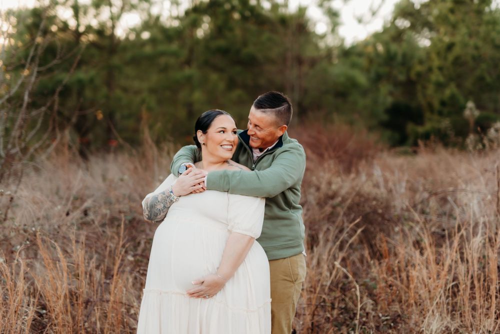 A romantic maternity photoshoot featuring a couple embracing in a field of dried grass.