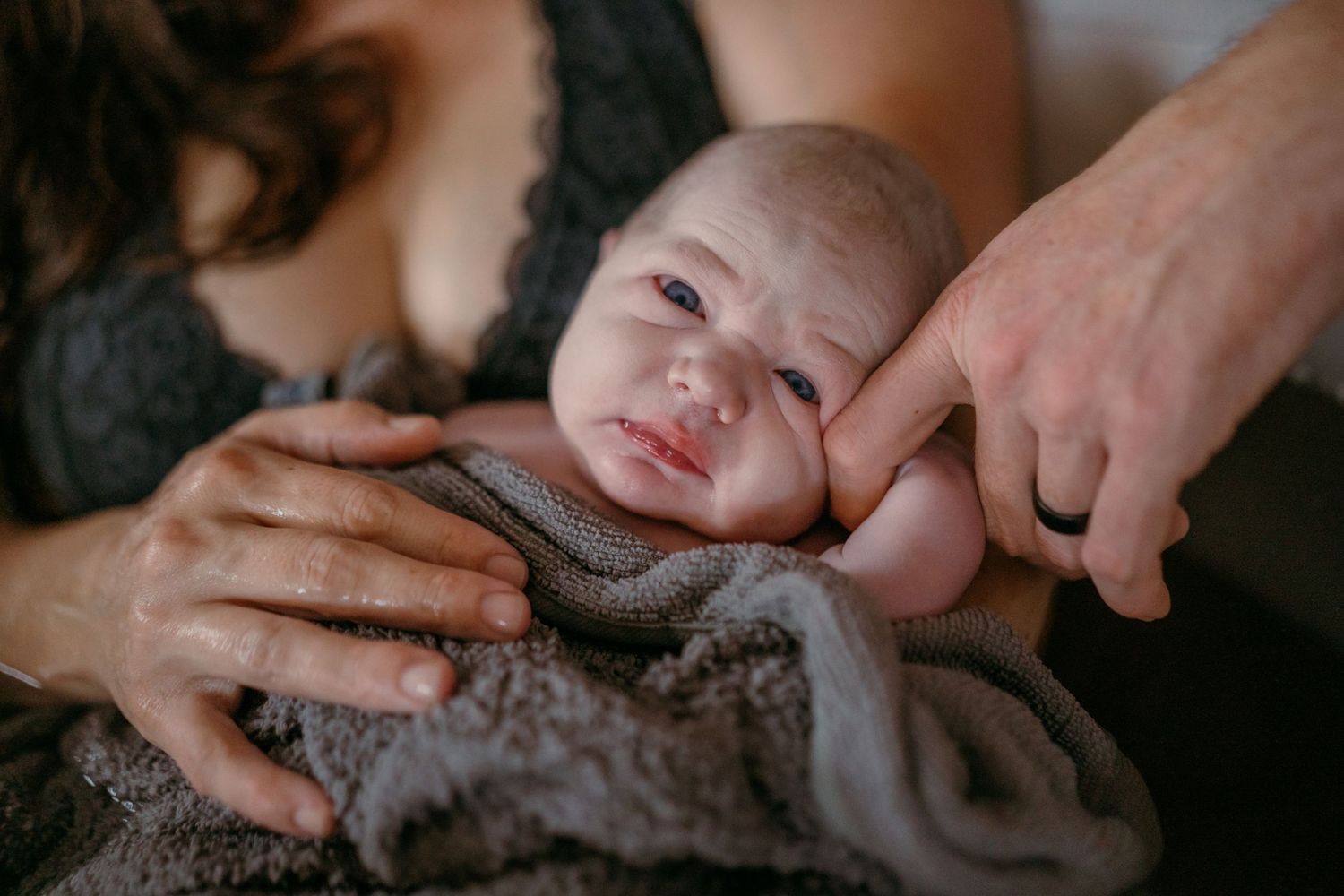 Close-up of a peaceful baby wrapped in a gray blanket with gentle hands providing comfort and care.