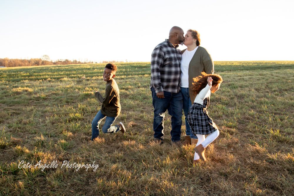 A family enjoys a warm evening together in an open field at sunset as kids play around their parents.  South Windsor, CT  Biracial family