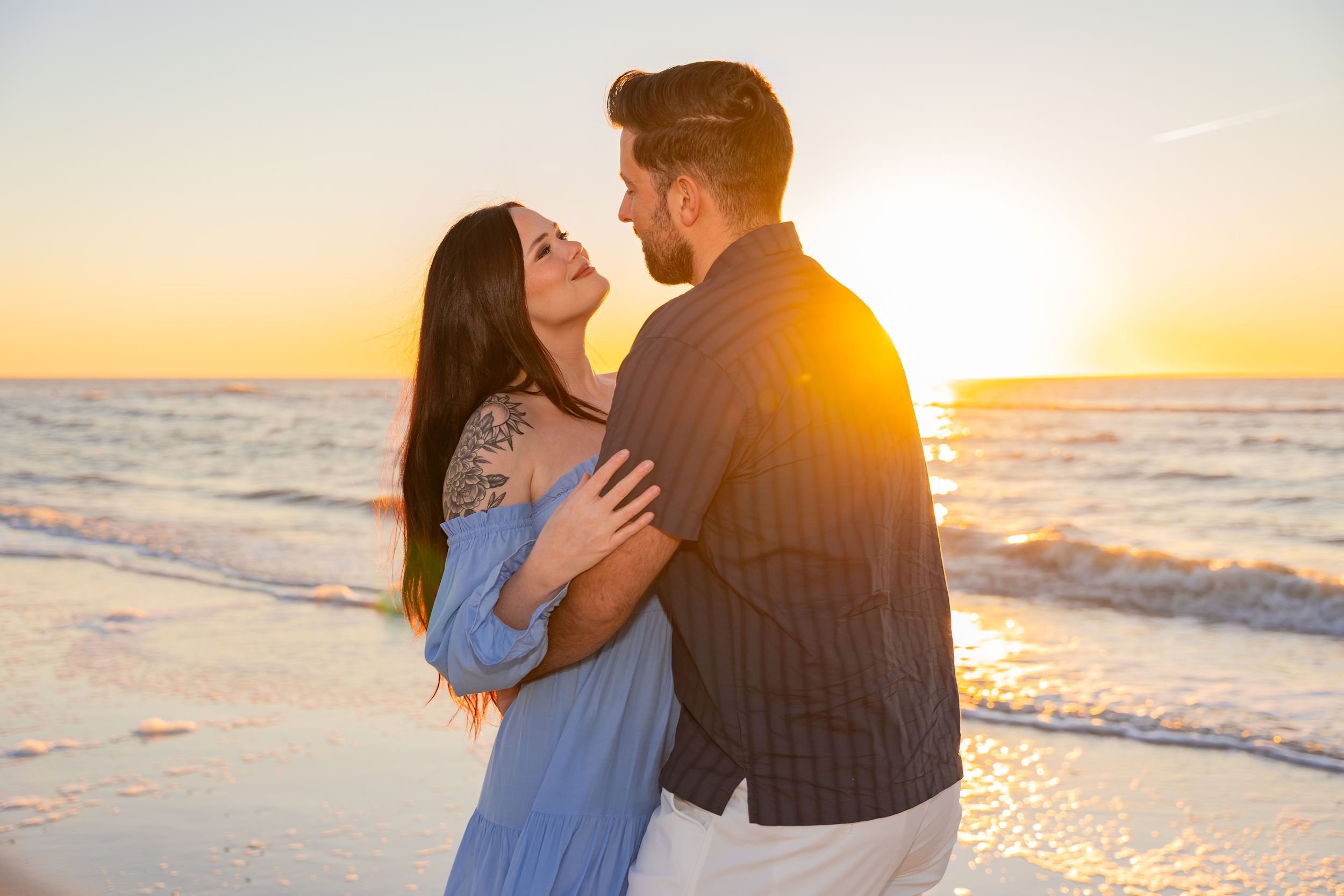 A couple embraces on a beach at sunset, silhouetted against the golden sky and ocean waves.