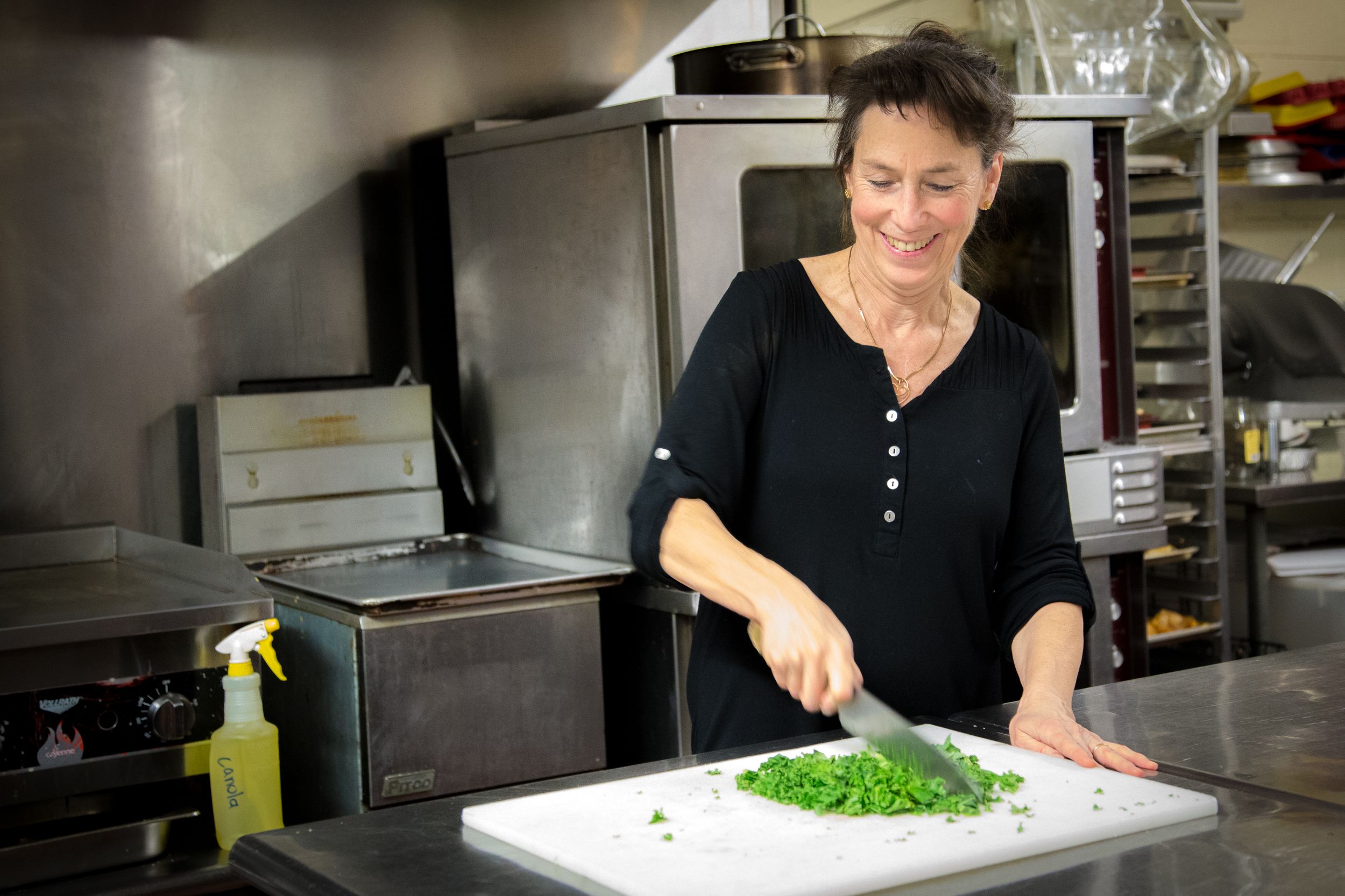 Fresh herbs being chopped on a white cutting board in a commercial kitchen setting.