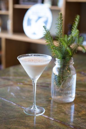 Creamy white martini cocktail served with fresh pine sprigs in mason jar decor.