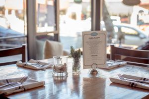 Elegant restaurant table setting with menu, glassware and fresh herbs in natural light.