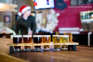 Flight of craft beer samples arranged on wooden serving board in varying shades.