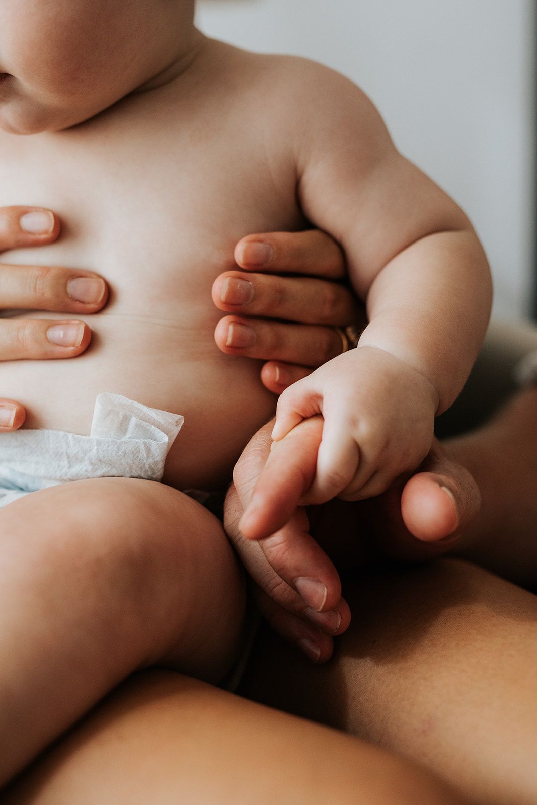 Close-up of a chubby baby in a diaper being held by an adult.