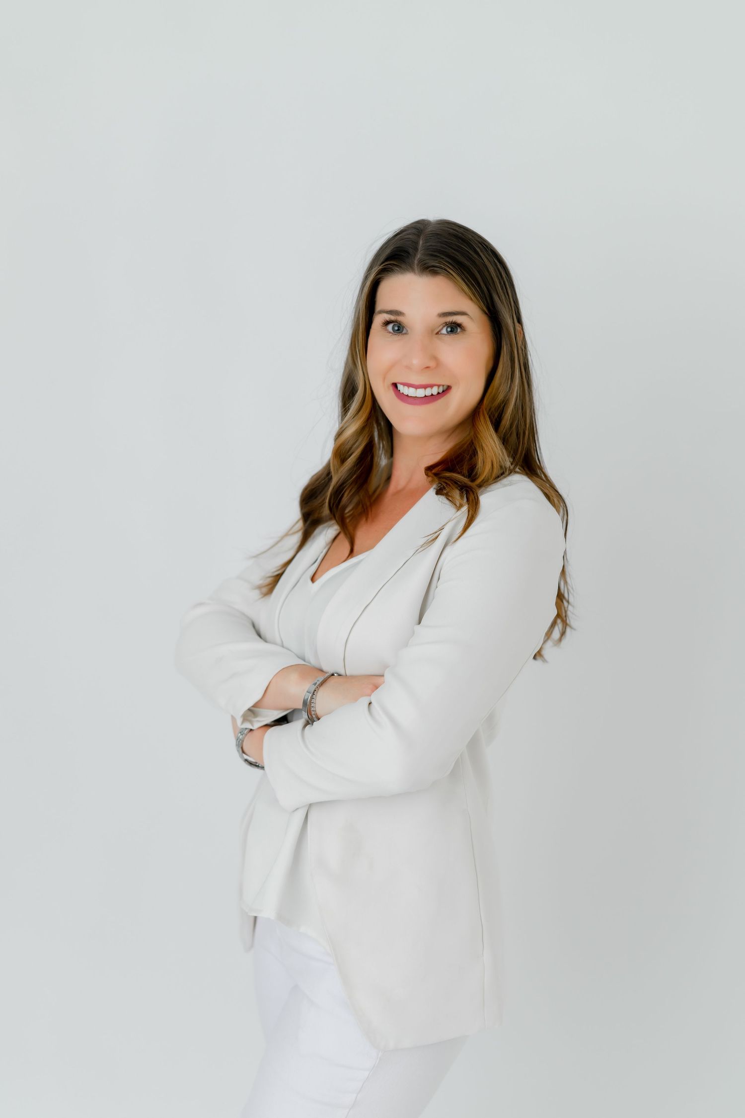 Professional headshot of person in white blazer with confident pose against neutral background.