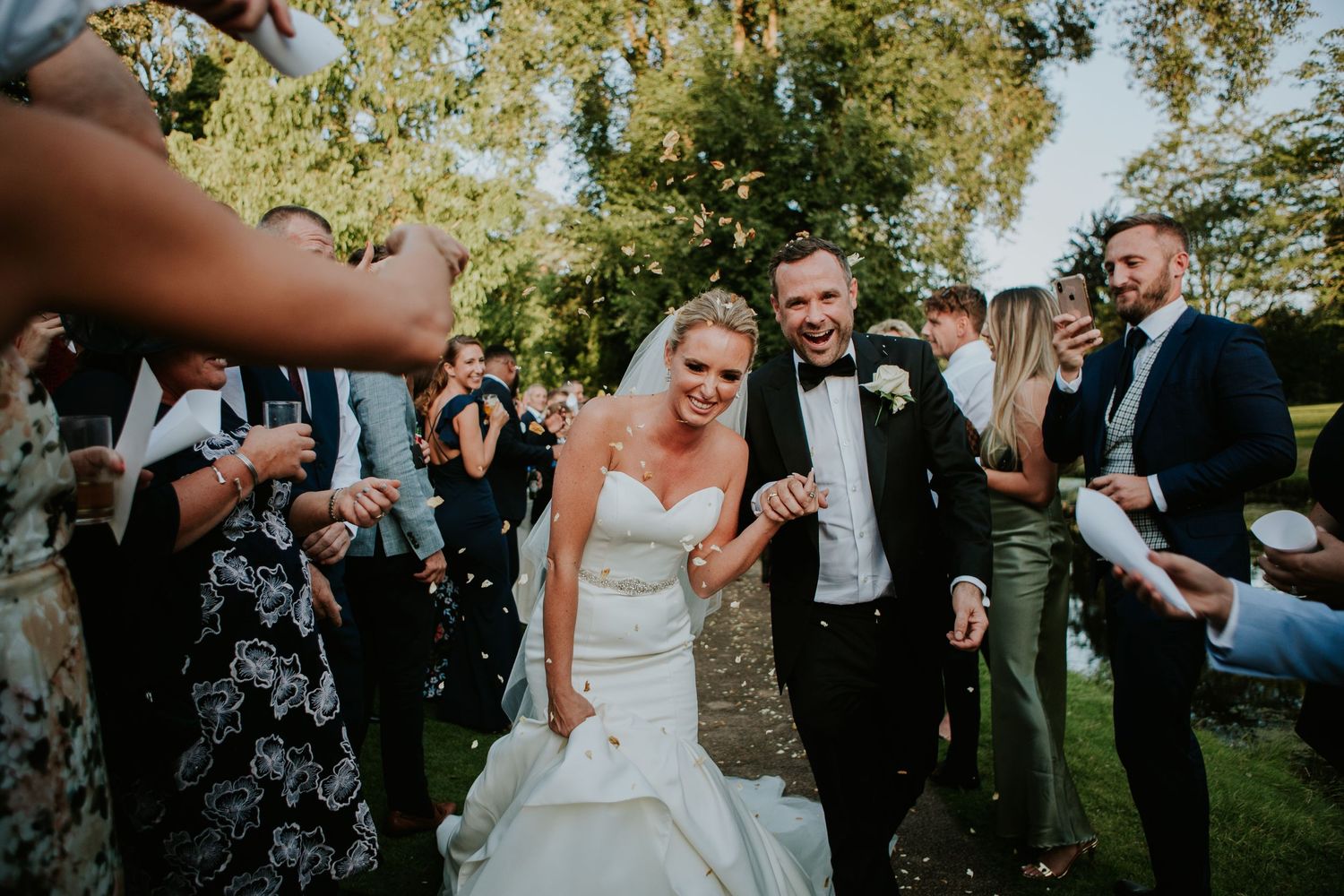 A joyous outdoor wedding celebration with guests throwing confetti in a garden setting.