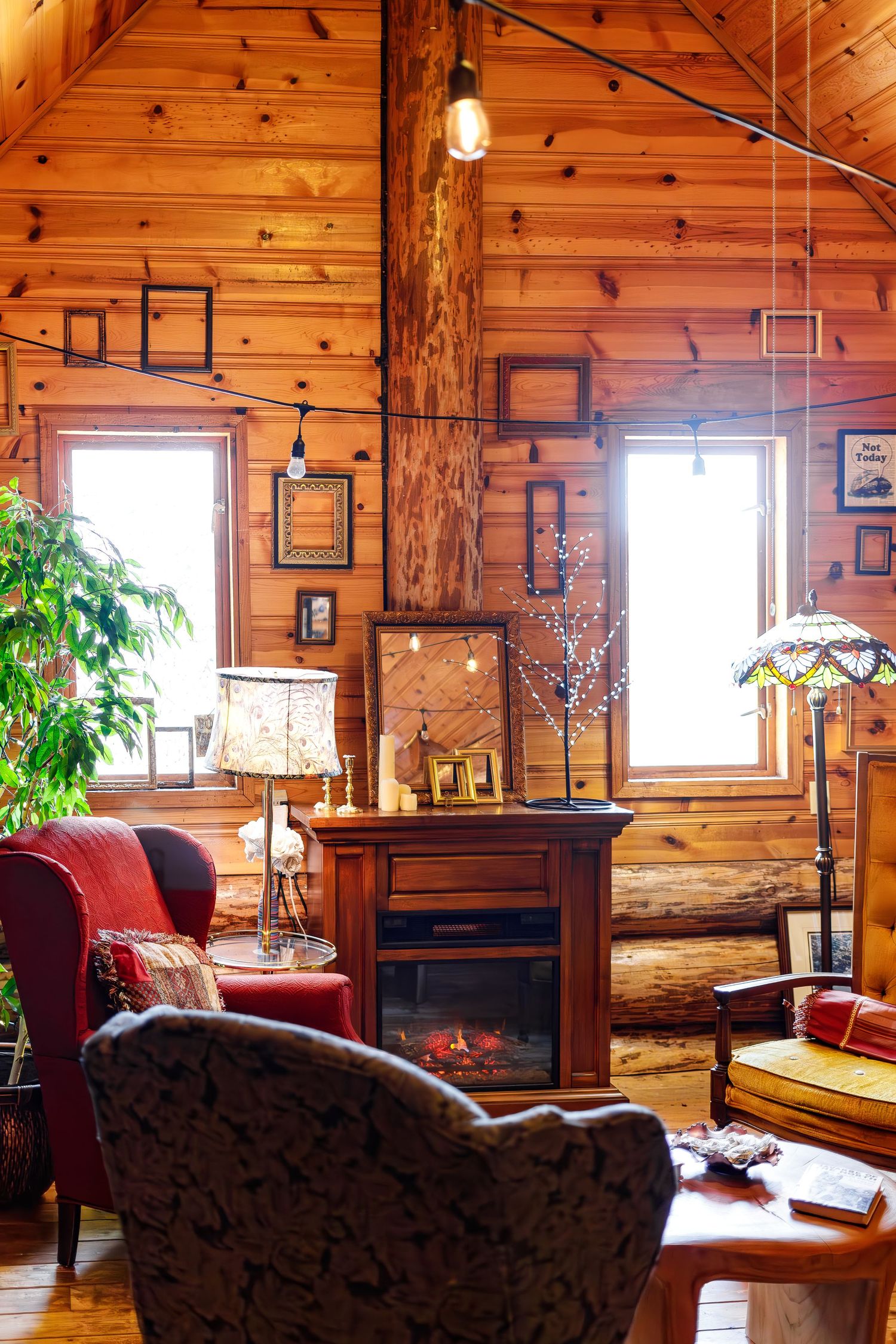 Cozy wooden cabin interior with comfy armchairs, rustic decor, and natural light streaming through windows.