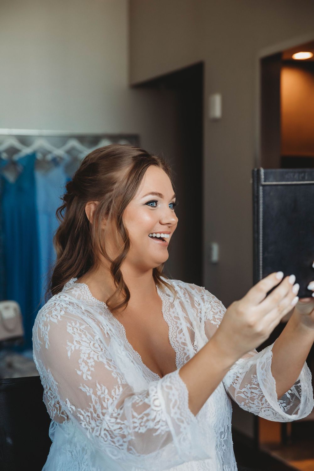 A joyful bride in lace getting ready on her wedding day while looking at her phone.