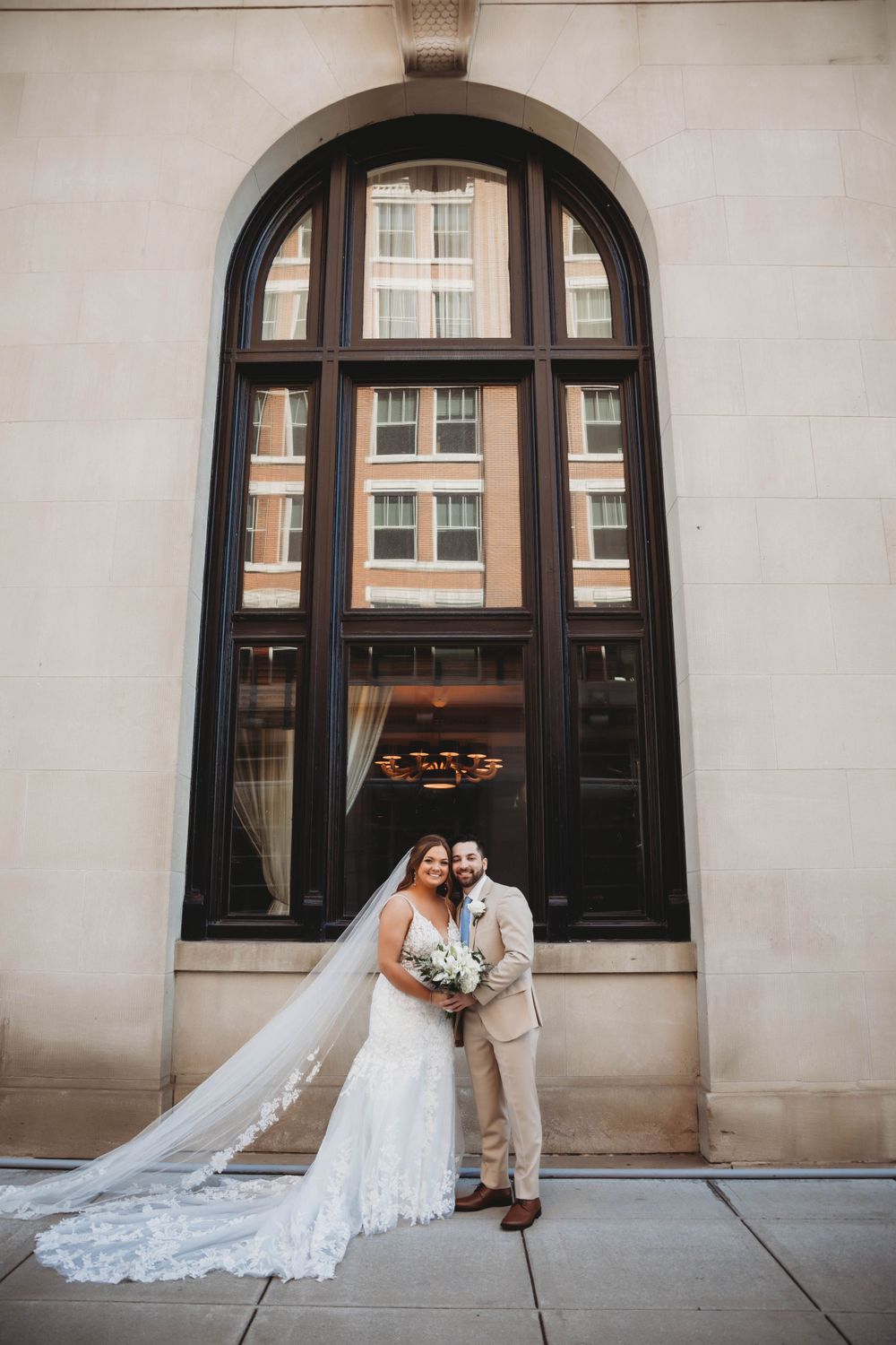 A wedding couple poses in front of a grand arched doorway of a historic building for their portrait.