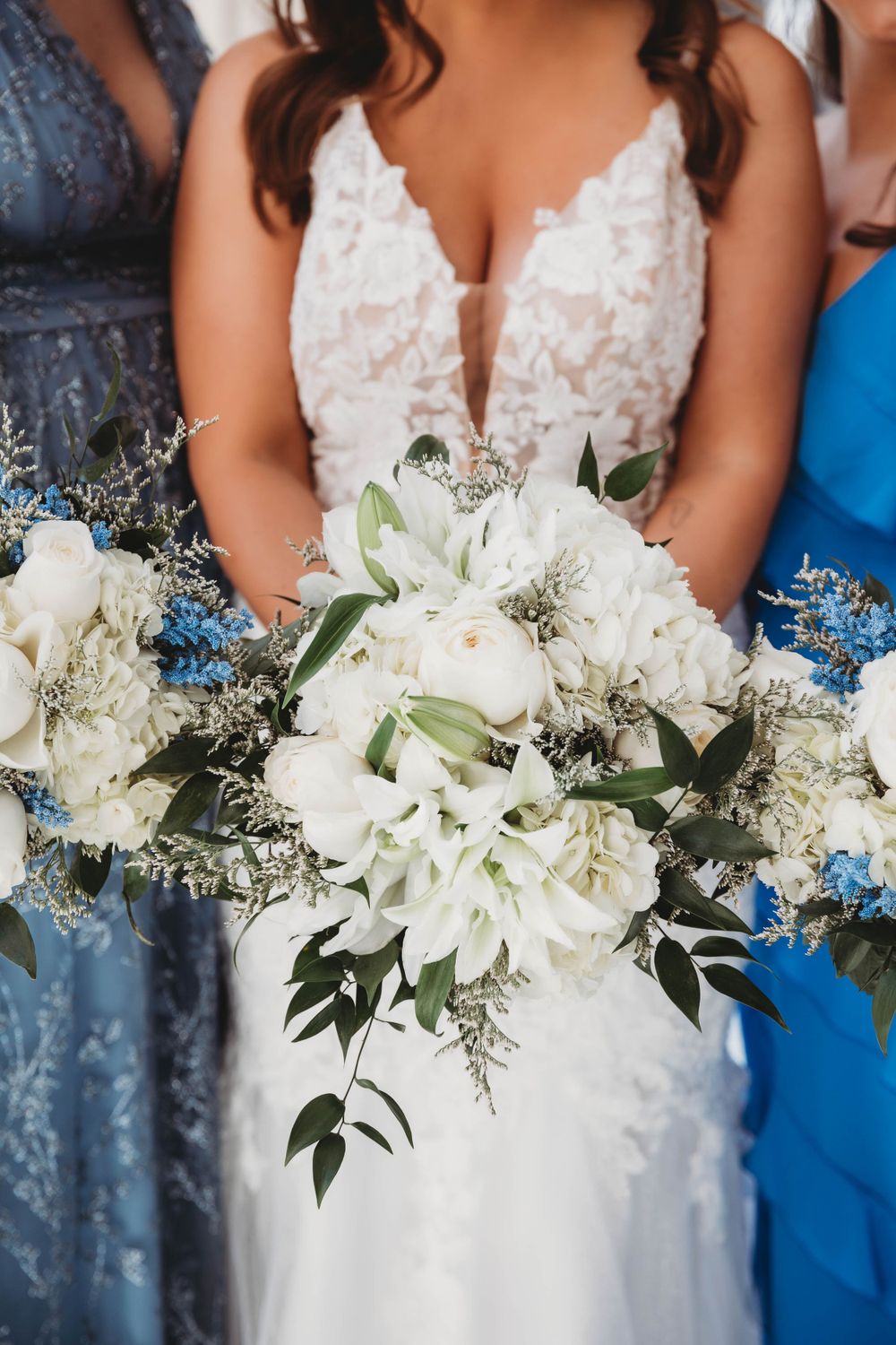 Close up of a bridal bouquet with white flowers and blue accents against a lace wedding dress.