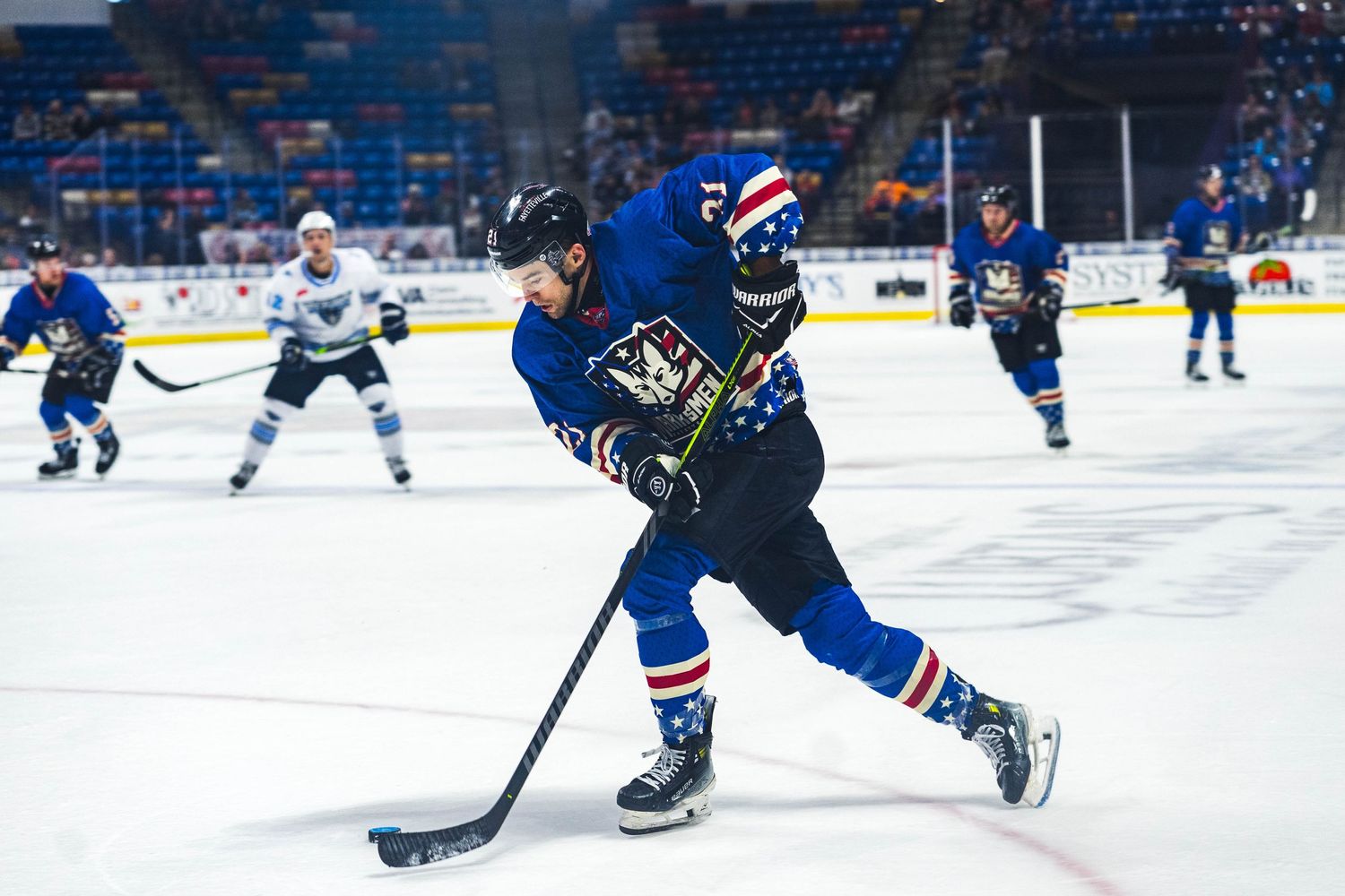 Hockey player in blue uniform carries puck during competitive game.