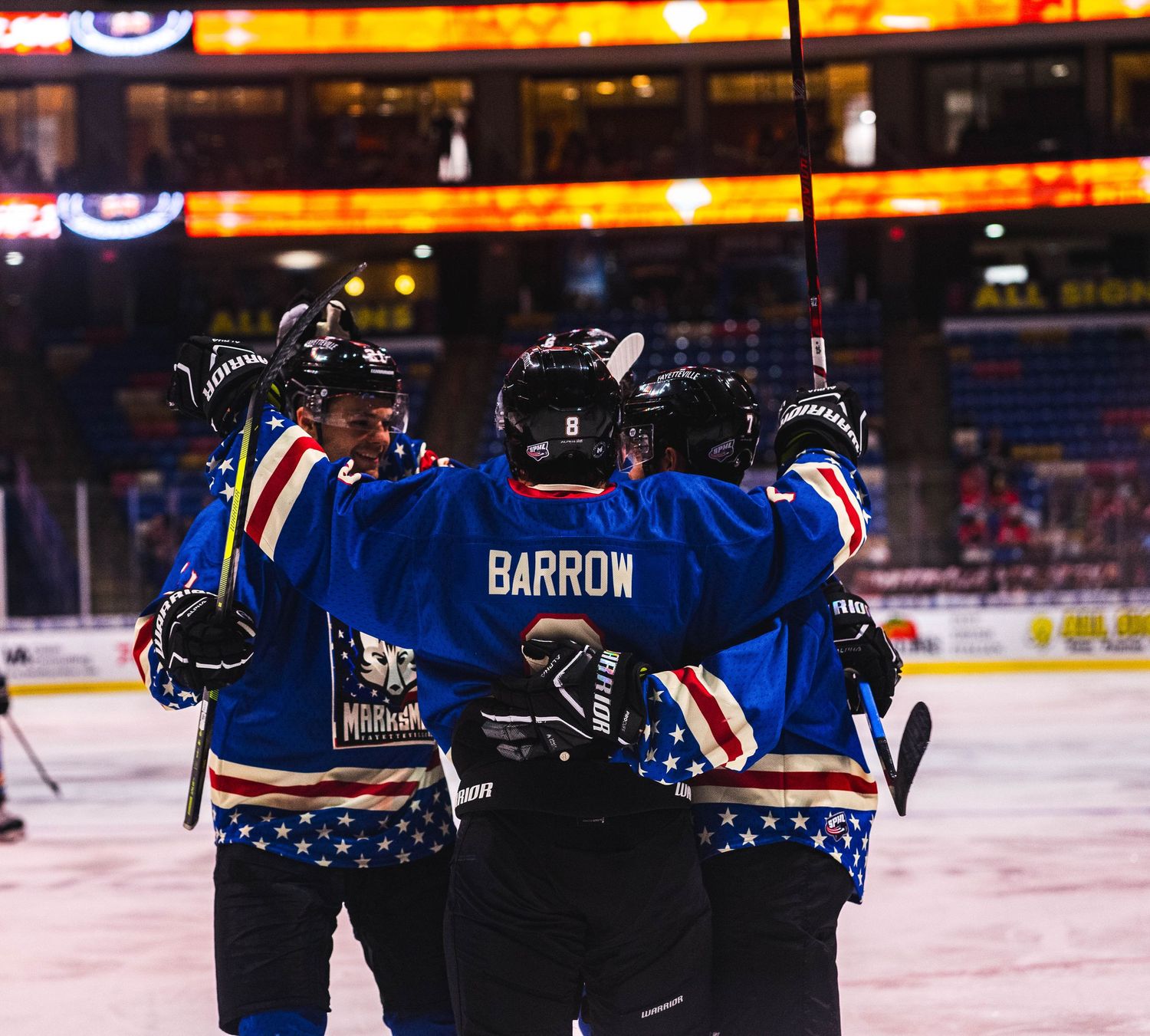 Hockey teammates huddle together on ice wearing blue jerseys with Barron nameplate.