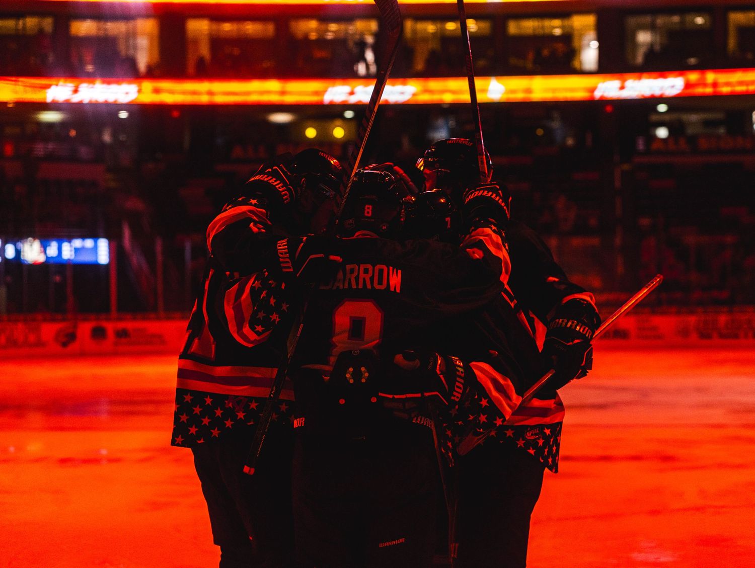Hockey players celebrate goal under dramatic red lighting in arena.