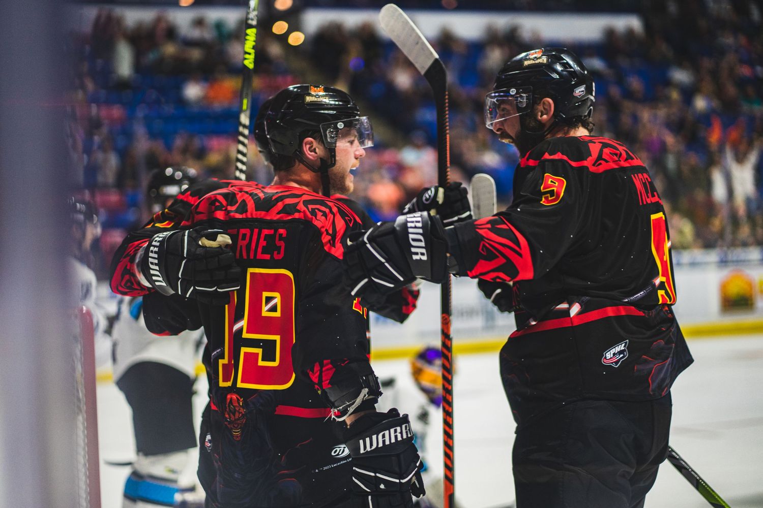 Hockey players in black and red jerseys celebrate after scoring a goal.