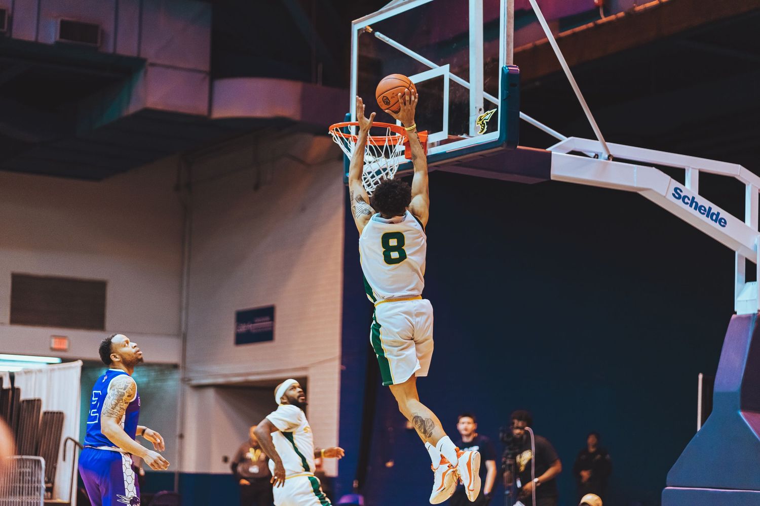 Basketball player in white jersey number 8 dunking ball during indoor game.