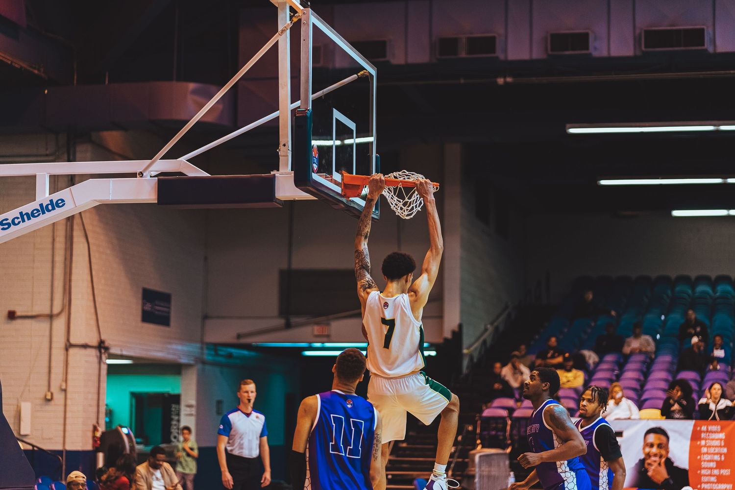 Player in white jersey performs powerful slam dunk during basketball game.