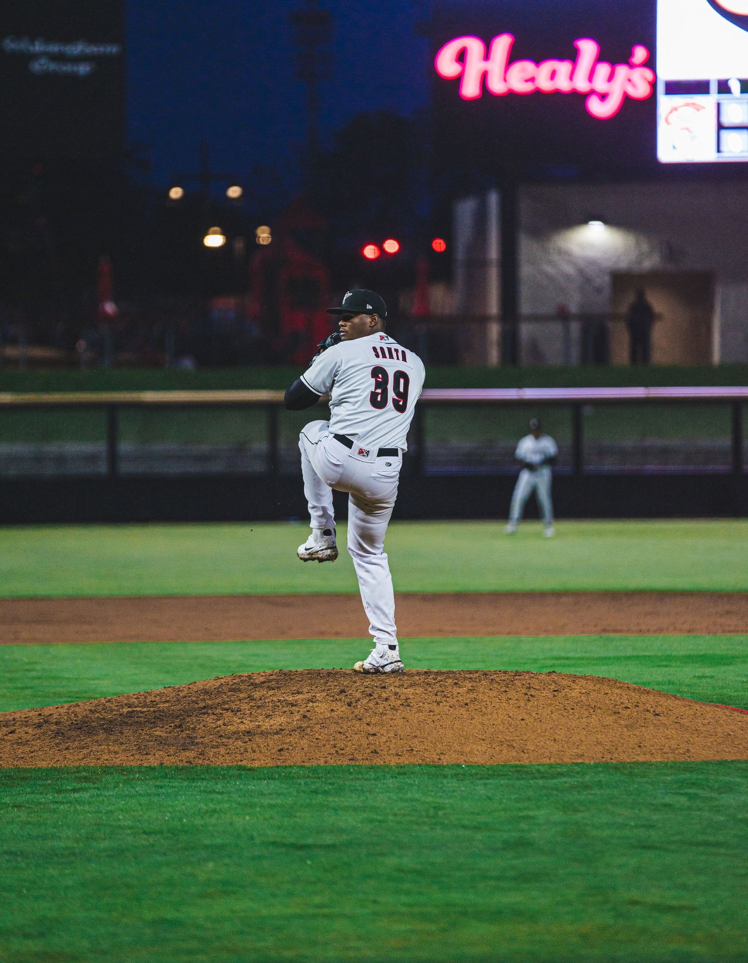 Baseball pitcher in white uniform number 99 throwing from mound at night.