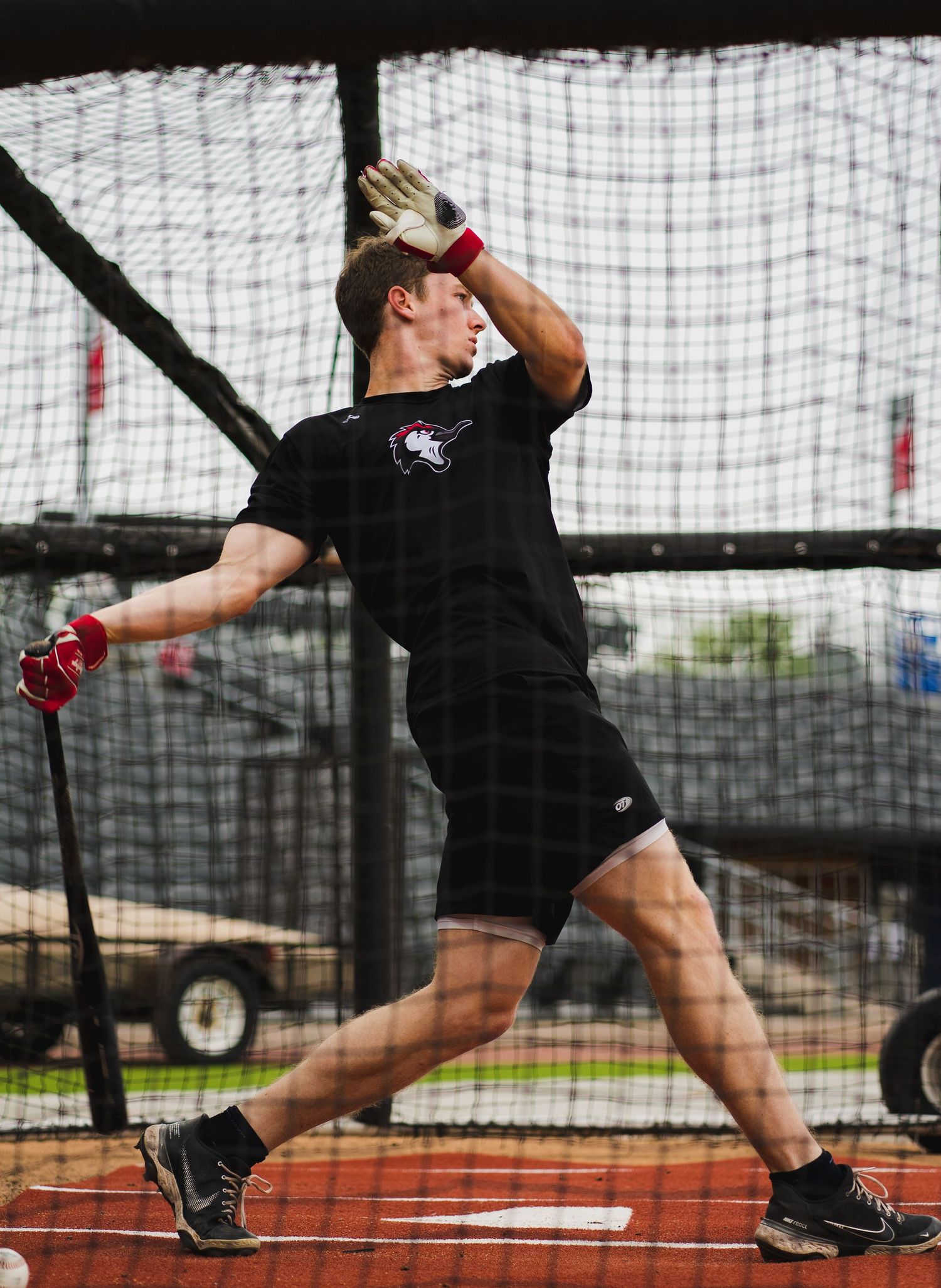 Athlete in black workout gear practicing discus throw form in a training cage.