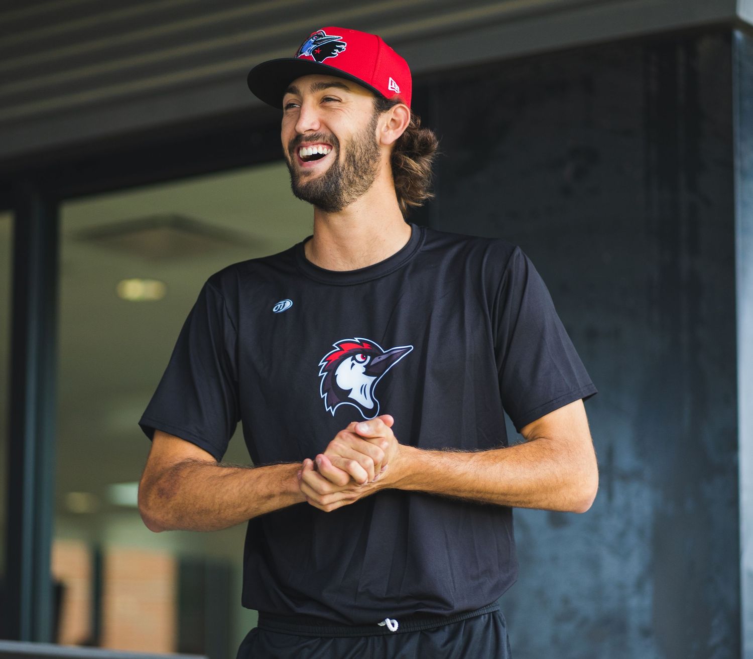 Baseball player wearing team merchandise smiles while standing outside stadium.