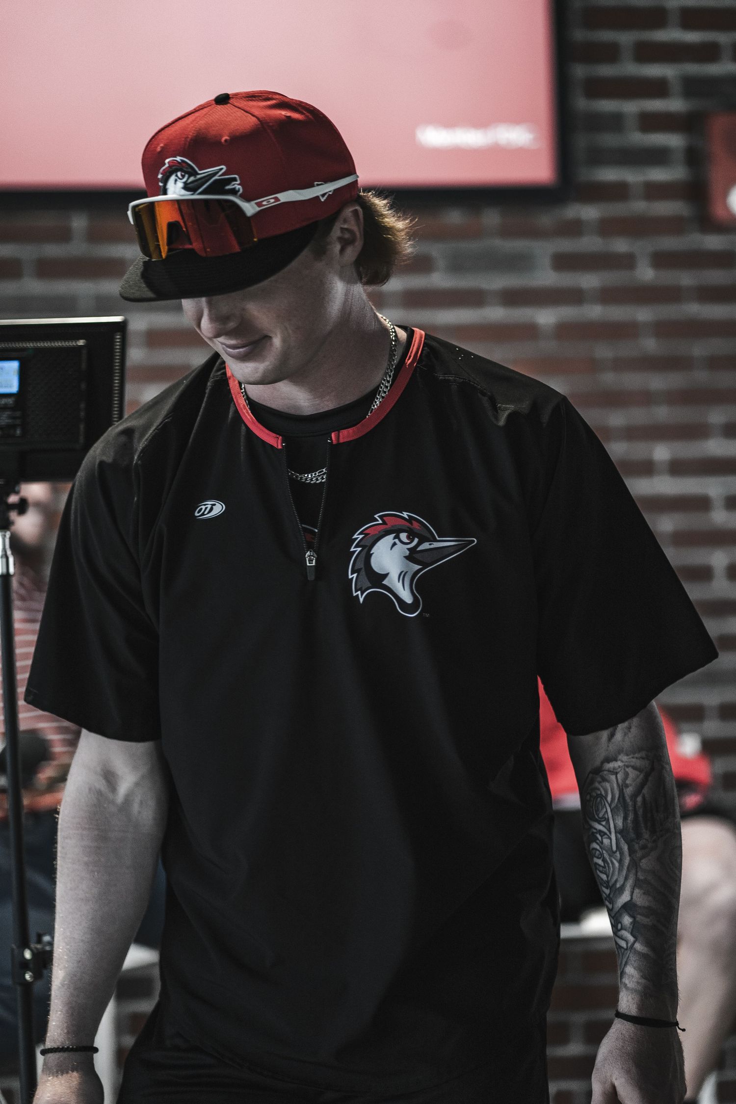 Sports team member wearing black uniform with hawk logo and red cap.